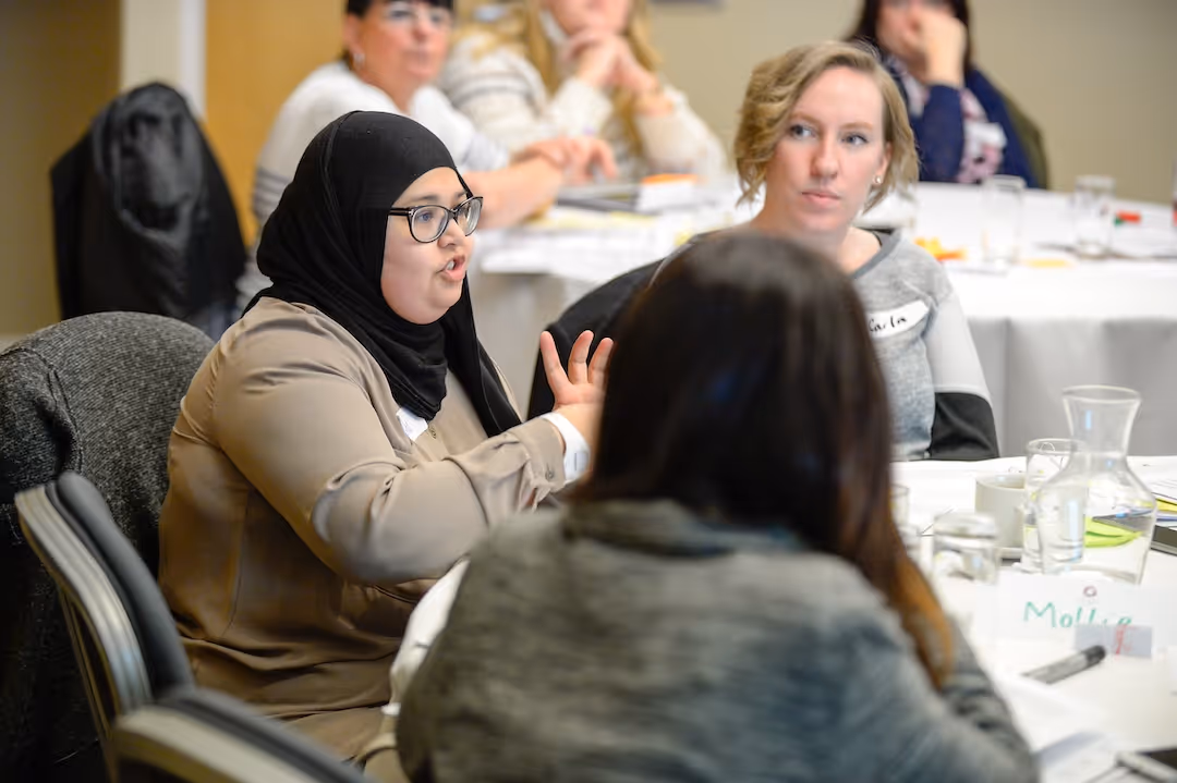 Teacher seated around a table engaged in a discussion during a meeting or workshop.
