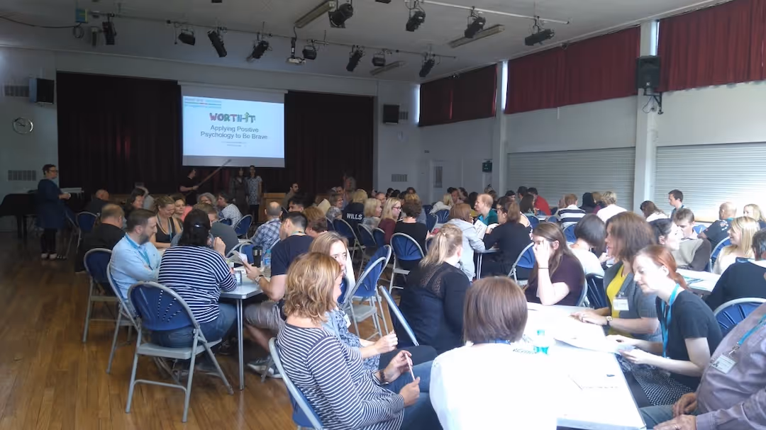 Group of people seated at tables attending a workshop in a large room with a presentation screen.