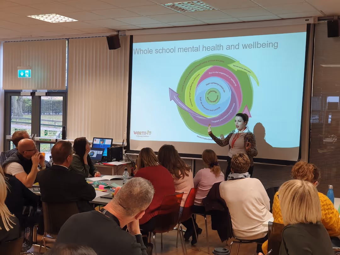 Liz Robson presenting a mental health and wellbeing diagram to an audience in a classroom setting.