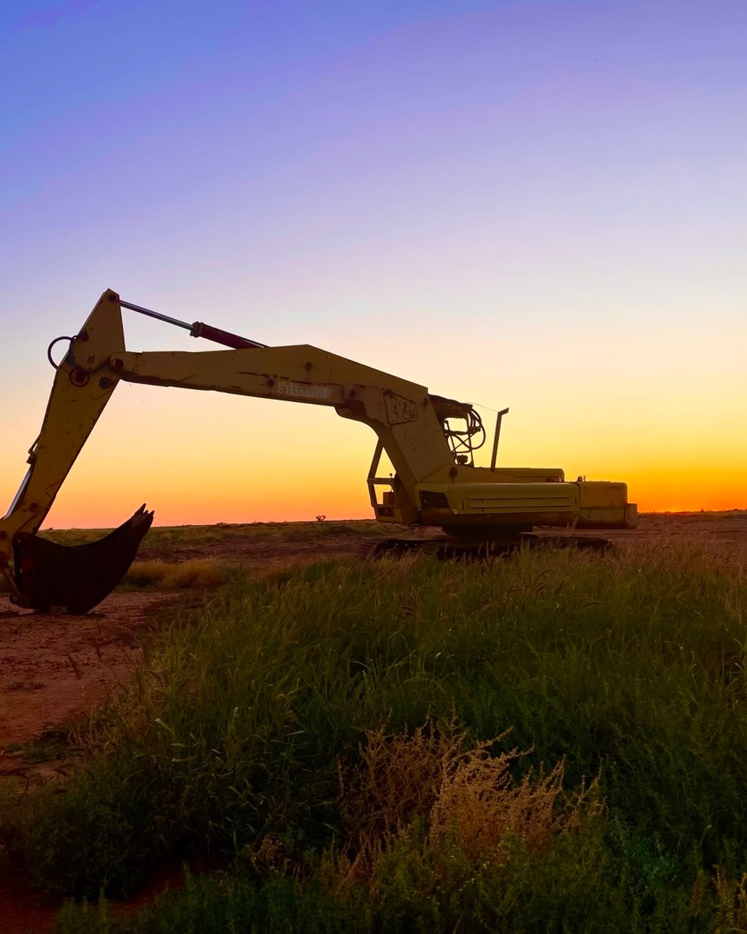 An excavator out in a field with the sunrise behind it