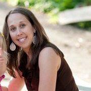 The photo is of a white woman with long dark hair. She is wearing a brown sleeveless blouse and silver earrings