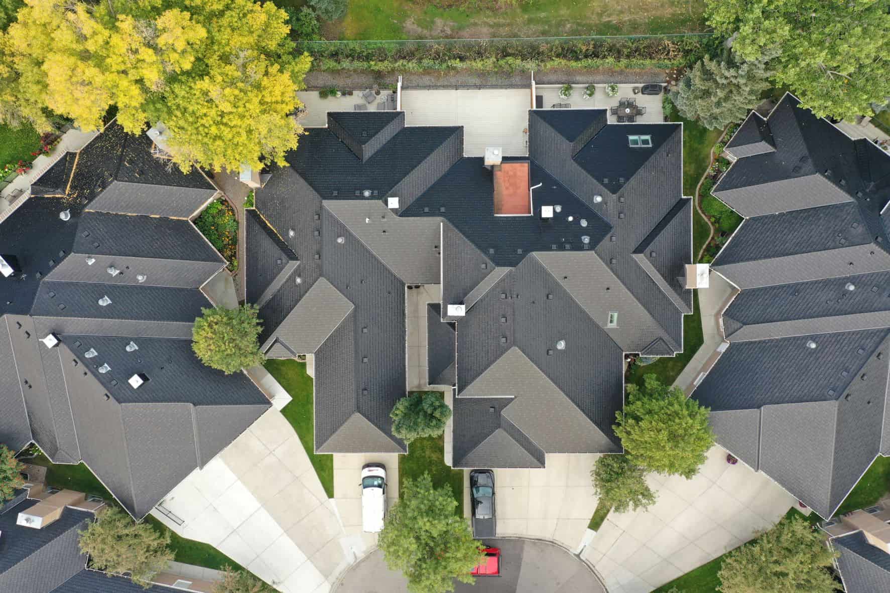 An aerial view of a housing complex with a distinctive arrow formation, featuring grey shingle rooftops and lush green trees on the perimeter.