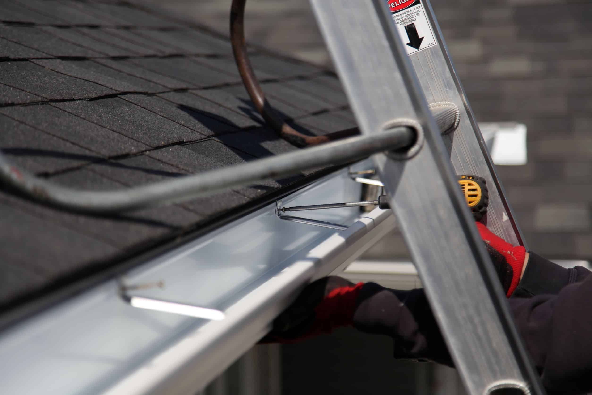 Close-up of a ladder leaning against a home's roof with a safety harness attached, indicating adherence to safety protocols during roof work.