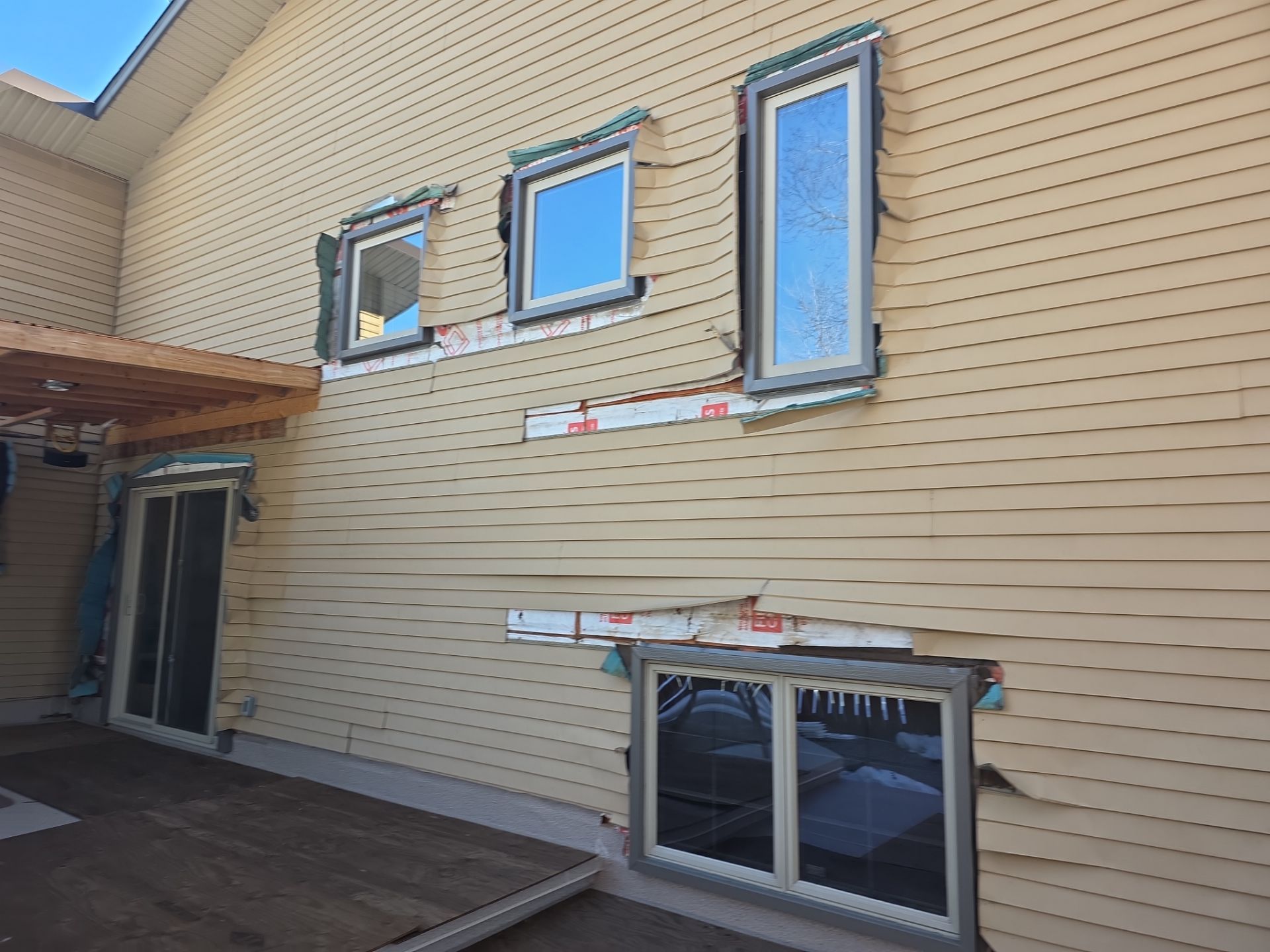 Damaged and missing vinyl siding around several windows on a home.