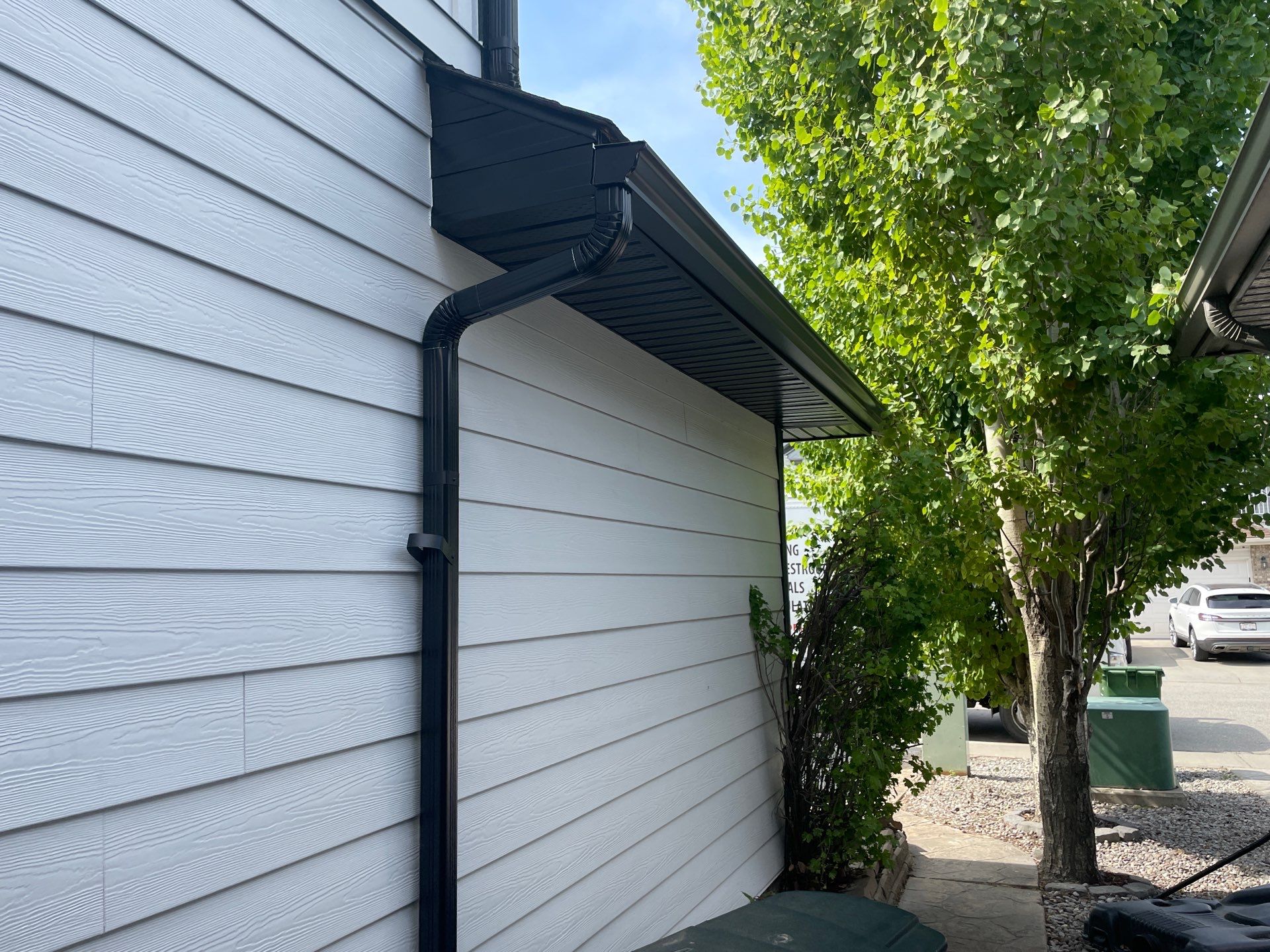 Black eavestrough and downspout installed on a home with white siding.
