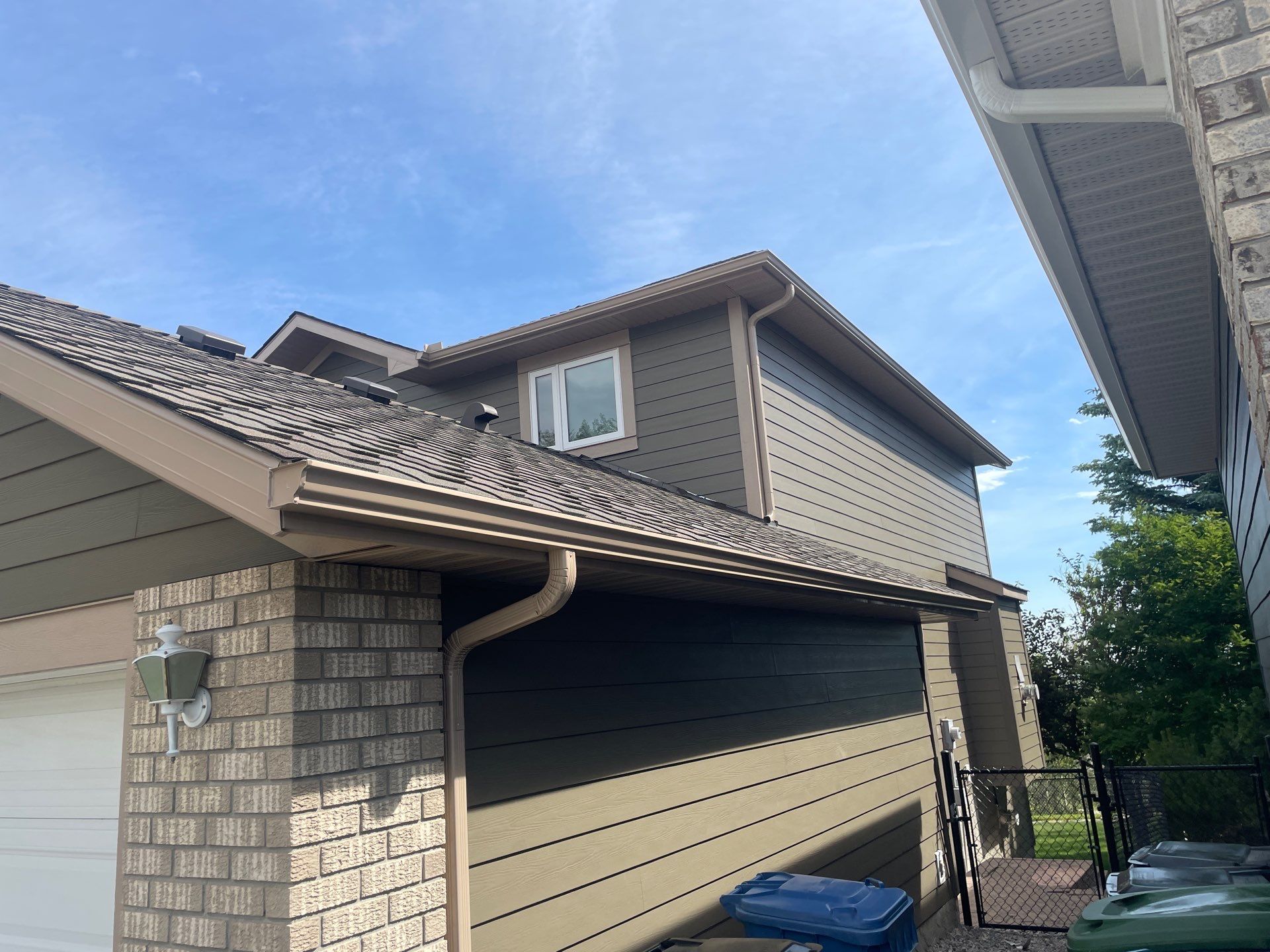 Beige eavestrough and downspout installed along a home’s roofline.