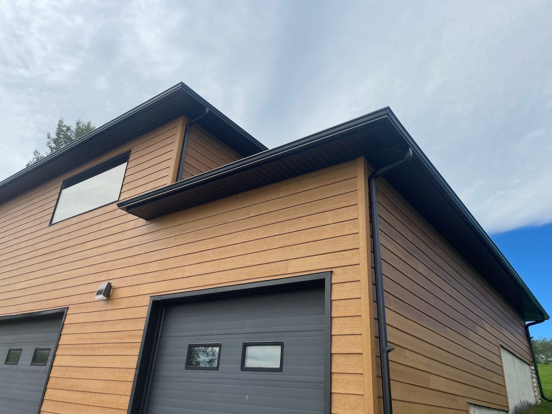 Black eavestroughs and downspouts installed on a garage with wood-look siding.
