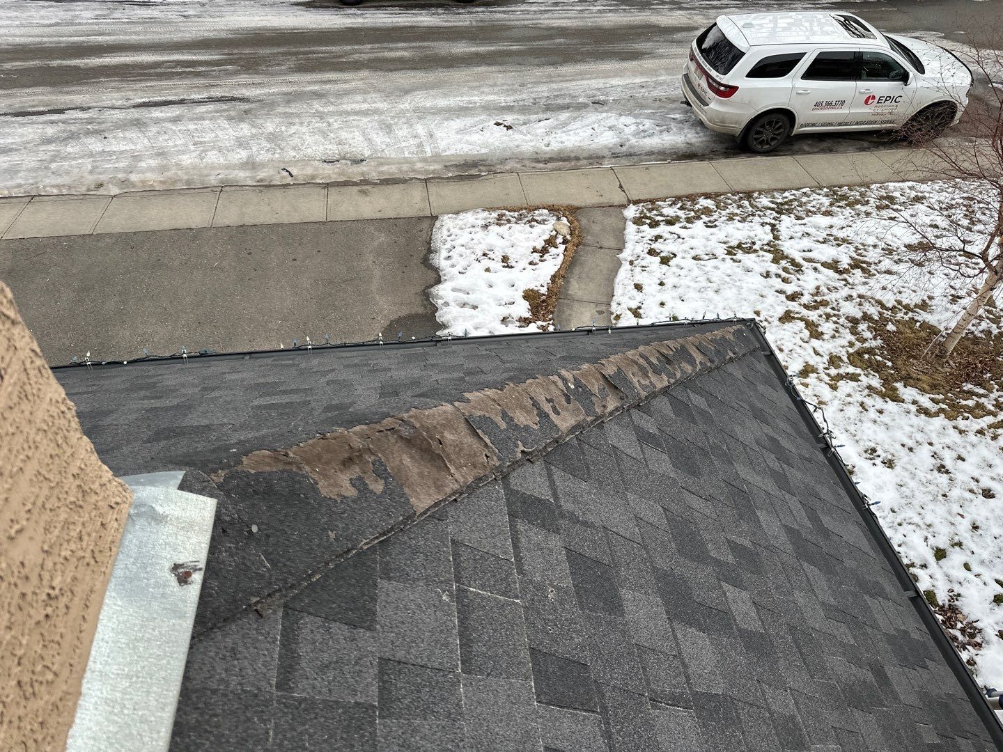 Worn and damaged ridge shingles on an asphalt roof during winter.
