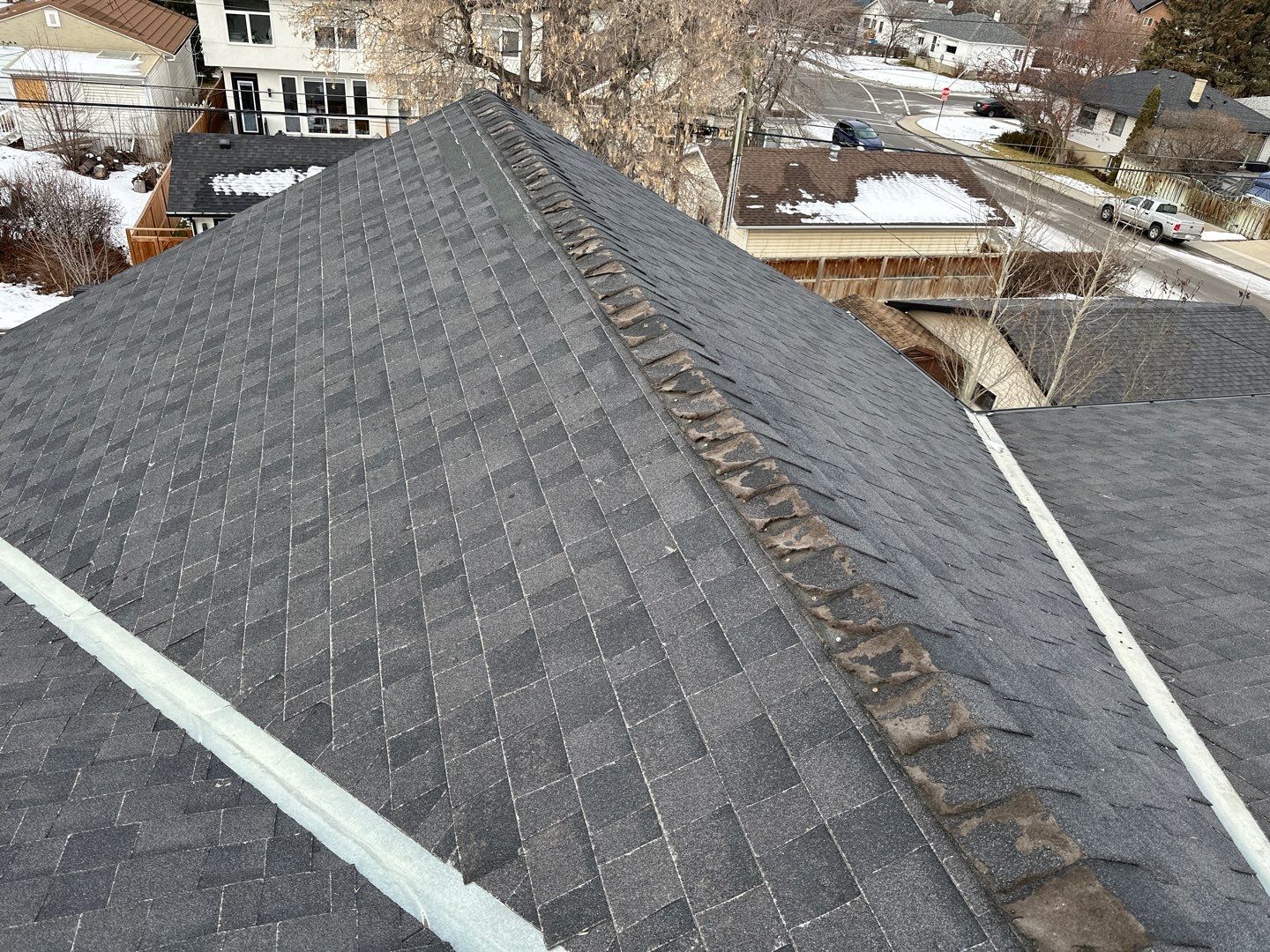 Severely worn ridge cap shingles on an aging asphalt roof.
