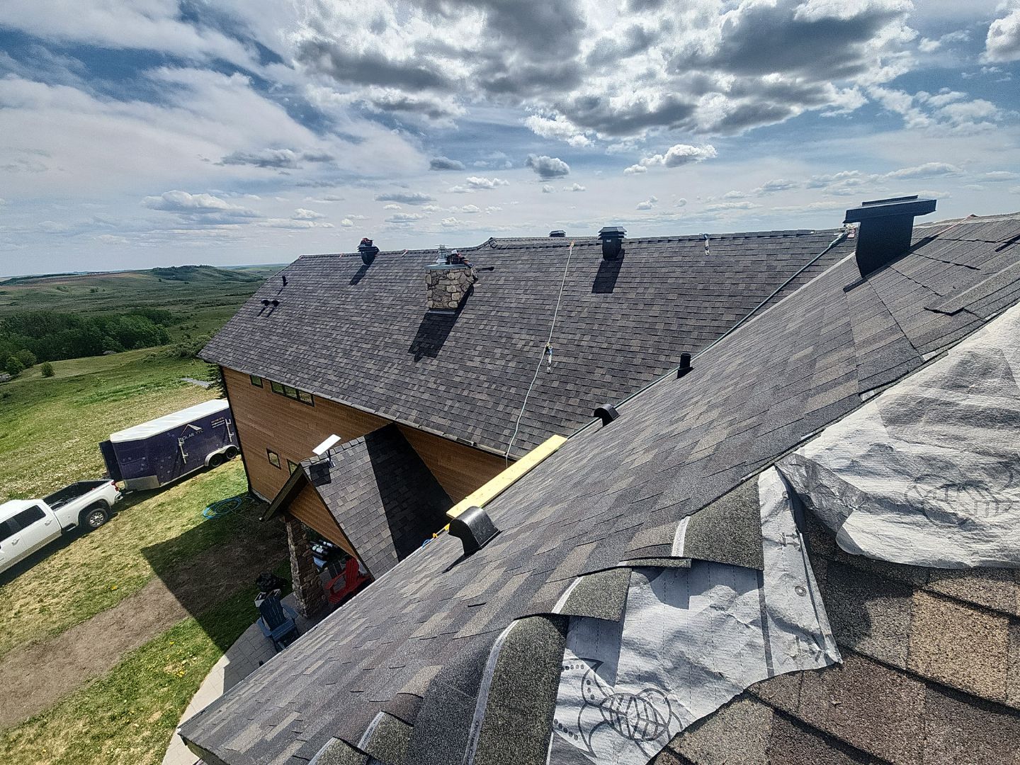 Asphalt roof repair in progress with exposed underlayment near a stone chimney.
