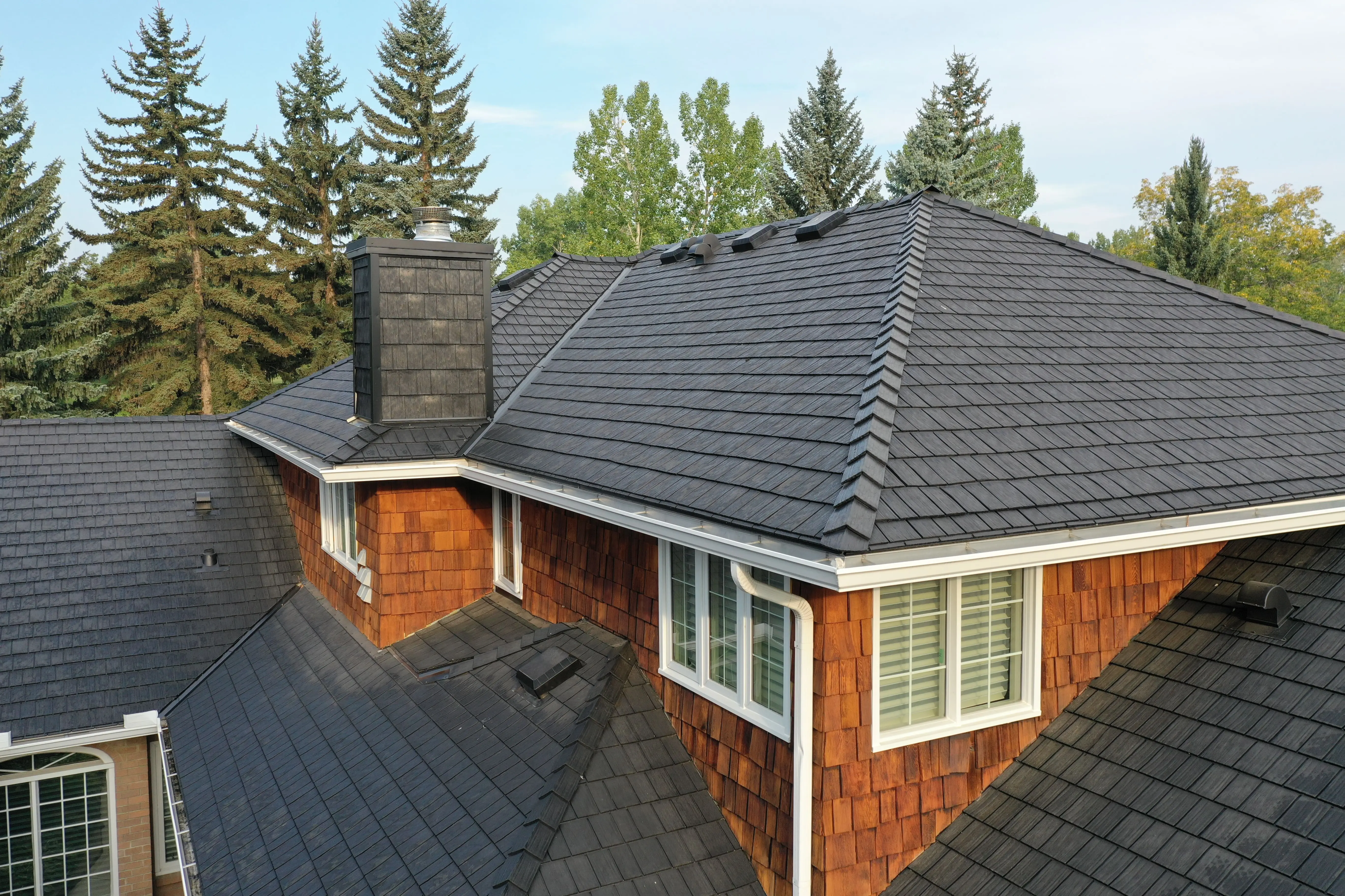 Aerial view of a home with dark grey shingle roofing and cedar shake siding.