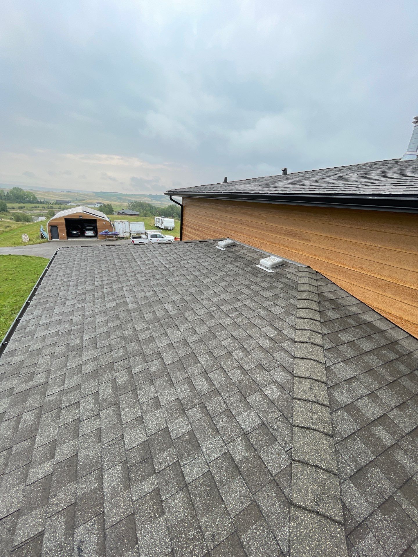 Aerial view of a home with dark grey shingle roofing and cedar shake siding.