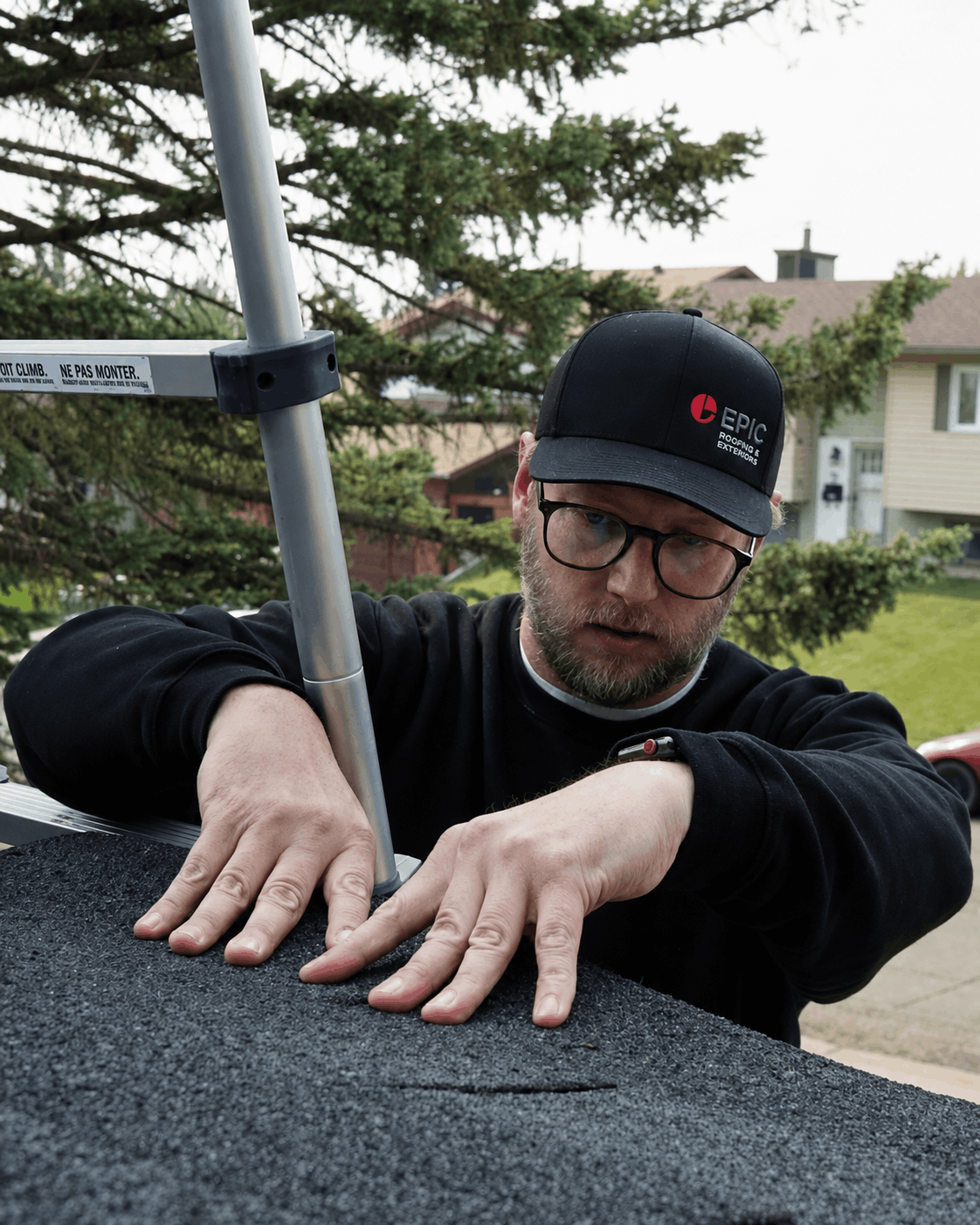 A roof inspector examining dark asphalt shingles up close.