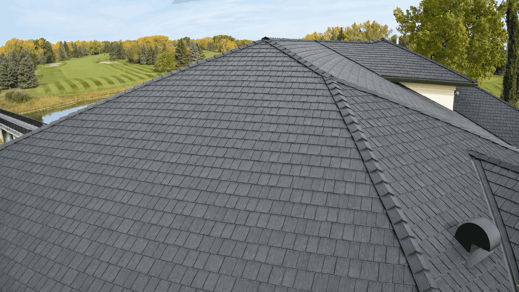 High-angle shot of a grey rubber shingle roof on a house next to a golf course.