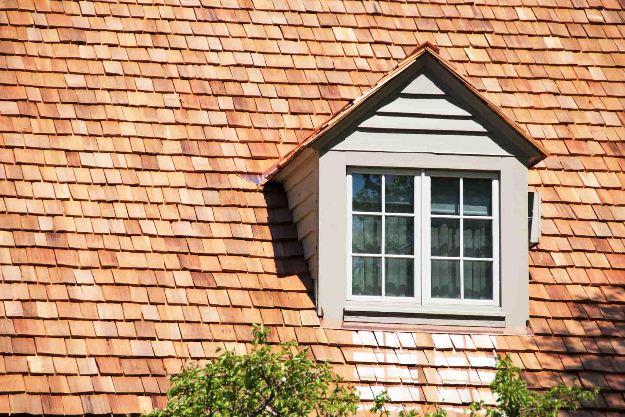 A small dormer window set into a warm, natural cedar shake shingle roof.