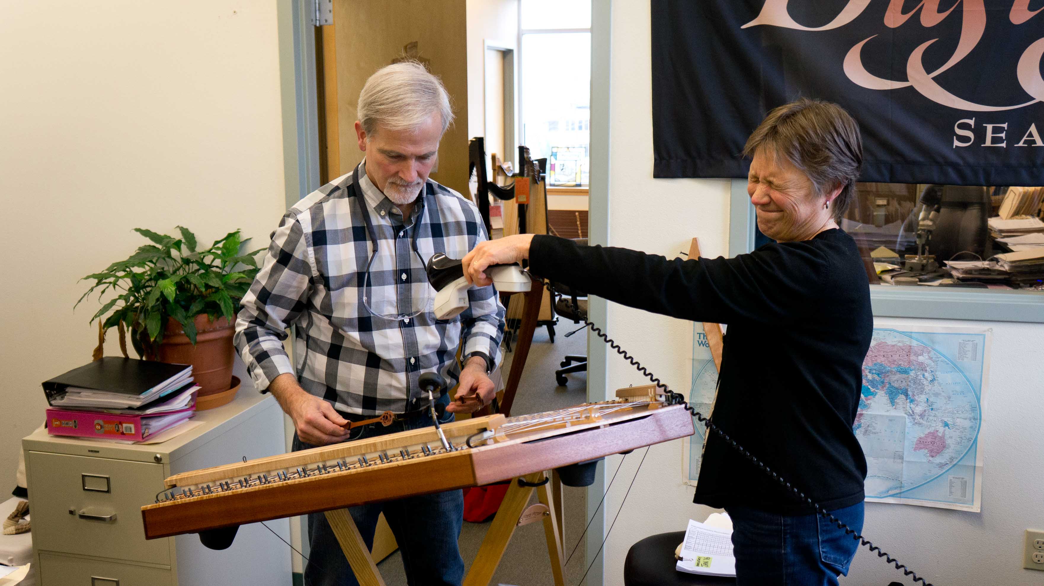 Owner Ray playing a D670 while owner Sue holds a phone headset above the instrument and cringes.