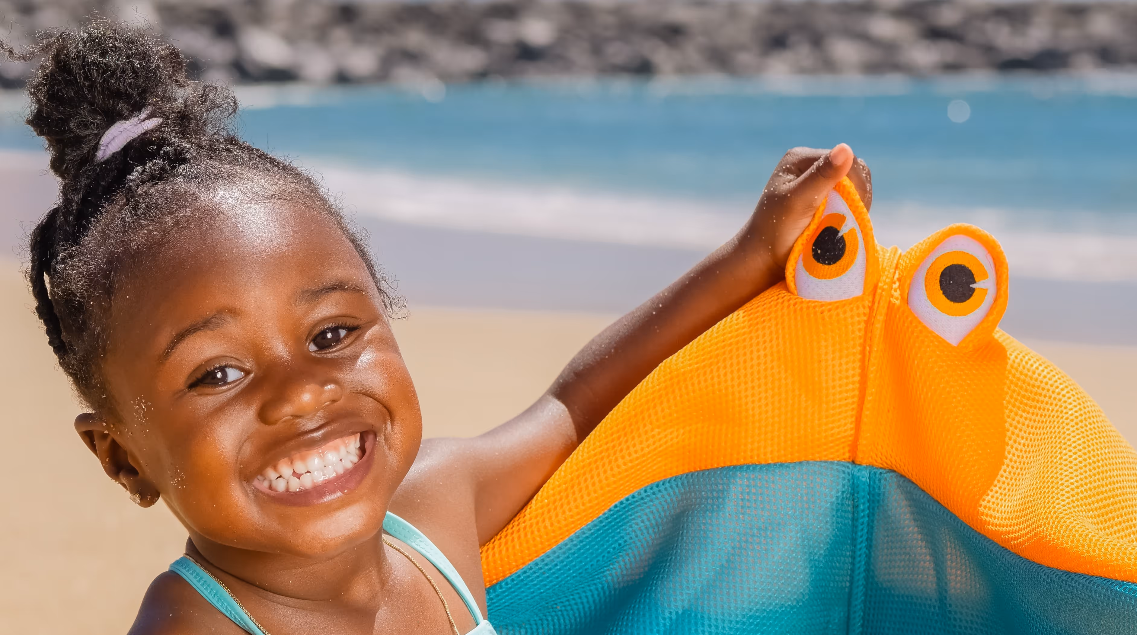 Mädchen auf Strand kneift das Auge eines Spielzeugs
