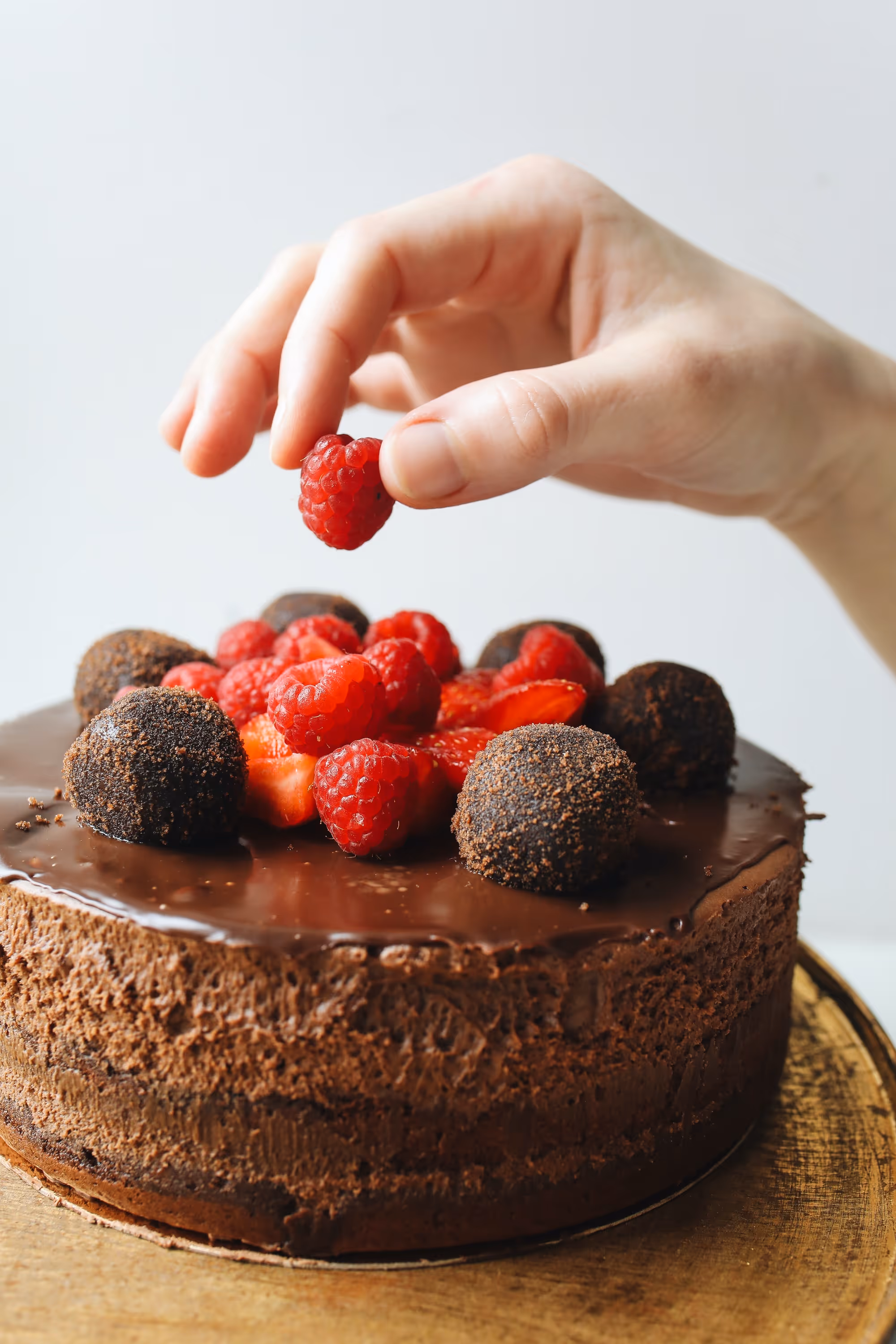 Hand reaching out for a raspberry atop a rich chocolate cake