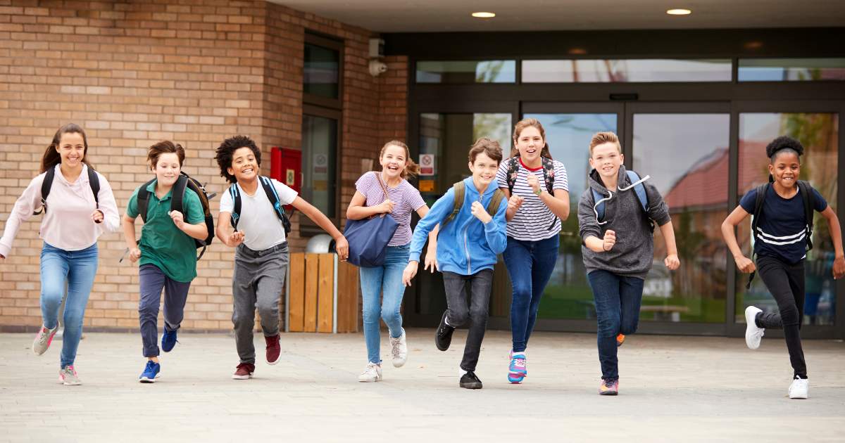 Group of young secondary school students running out of a school building happy