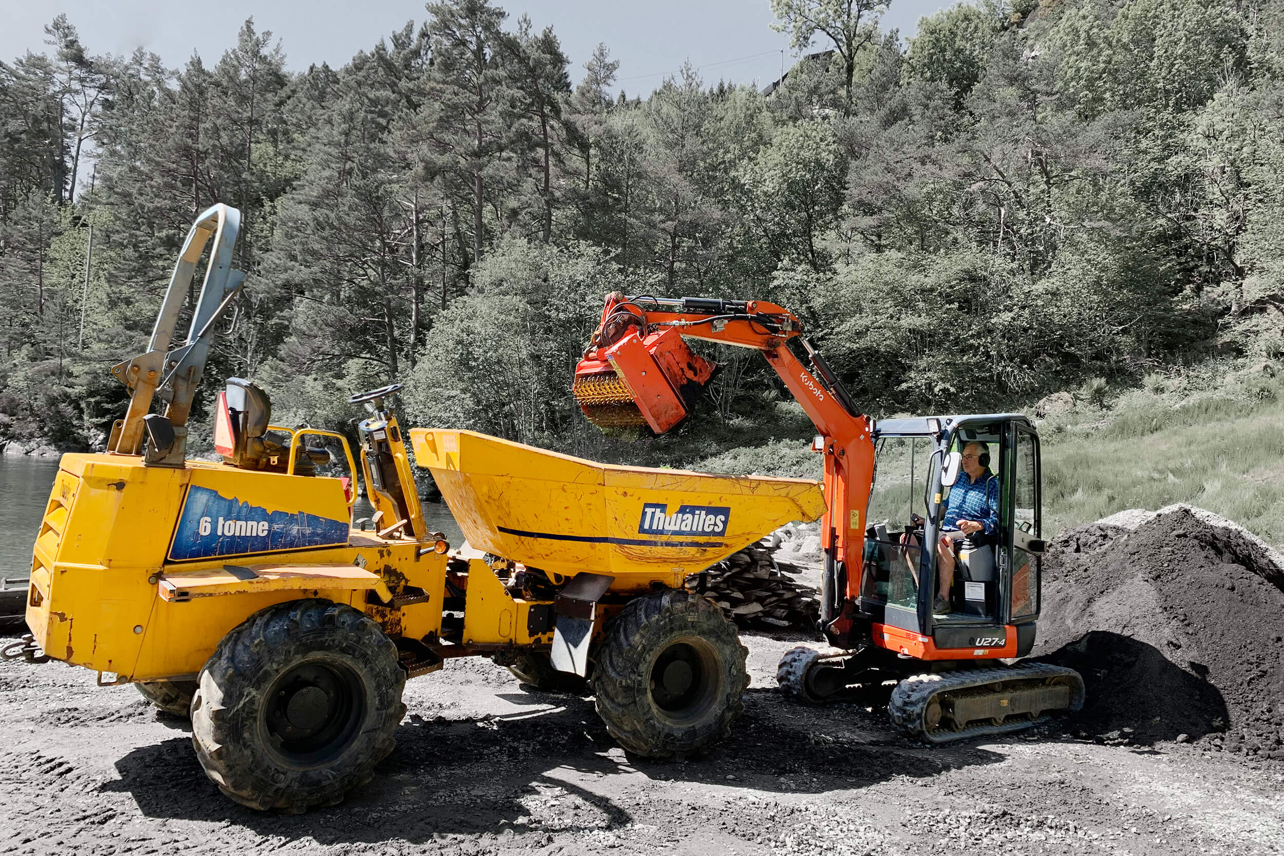 Mann i minigraver tømmer masse i minidumper