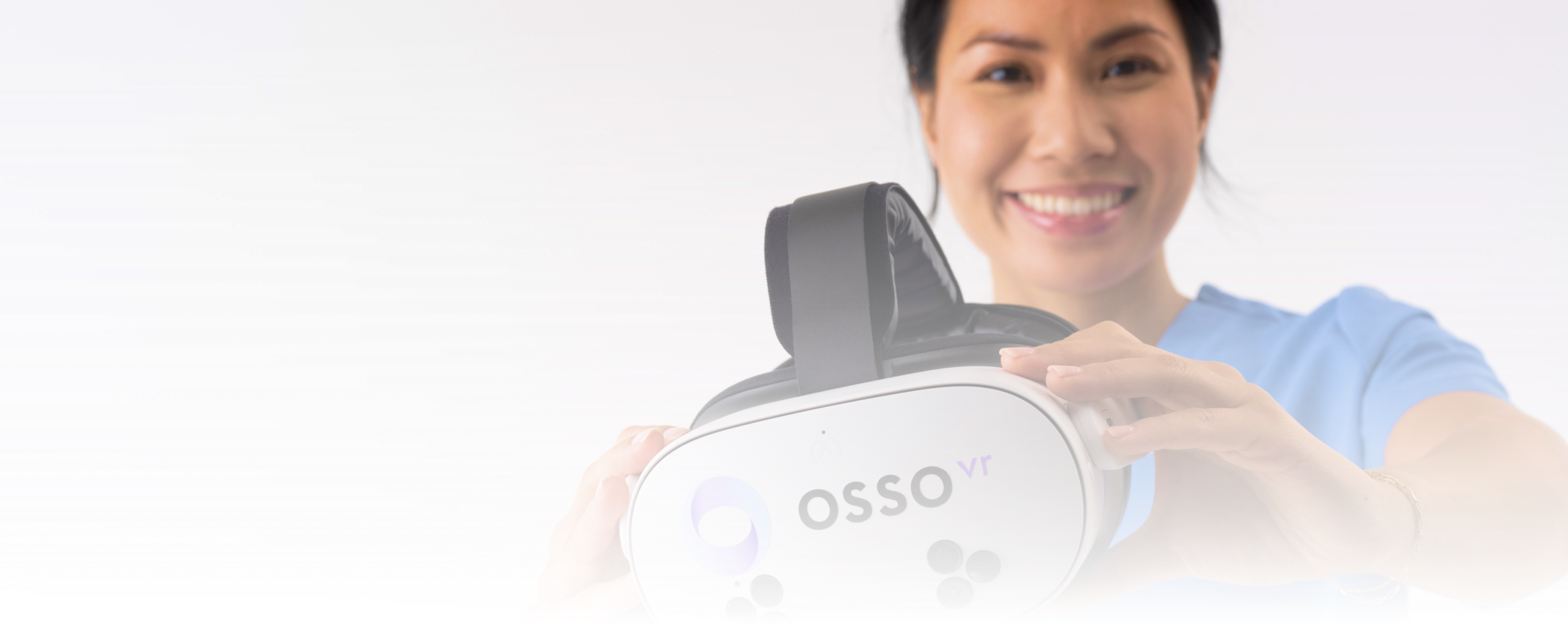 Smiling woman in blue scrubs holding a white Osso VR virtual reality headset.