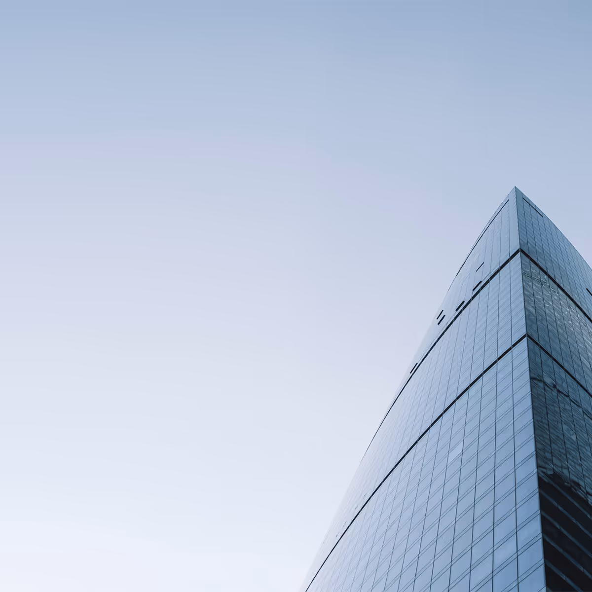 Blick von unten auf ein modernes, hohes Glasgebäude mit klarem Himmel im Hintergrund.