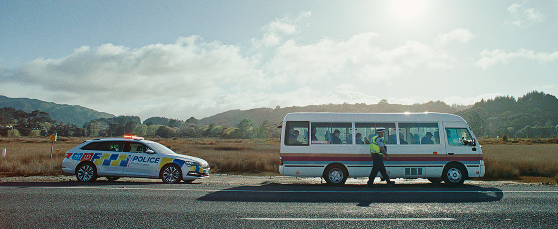 Two police officers seated in a car, one holding a radio and looking out the window.