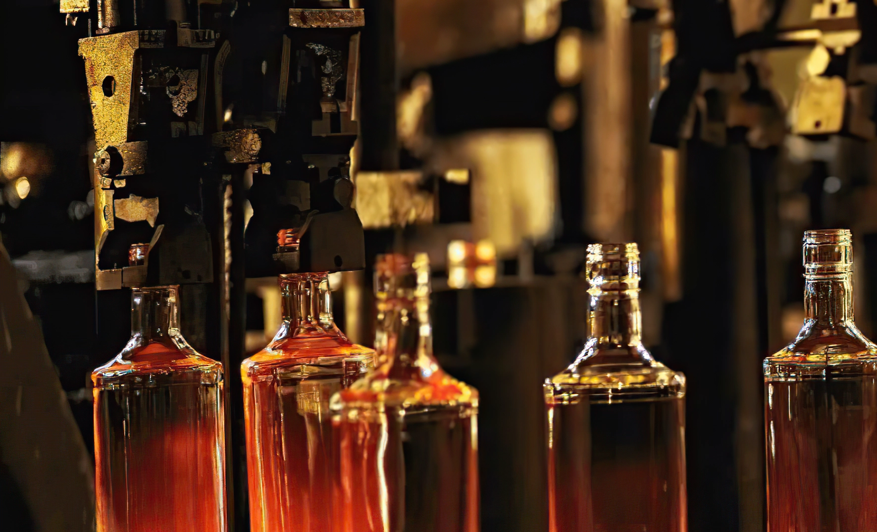 Close-up of glass bottles being shaped and heated in an industrial glass manufacturing process.