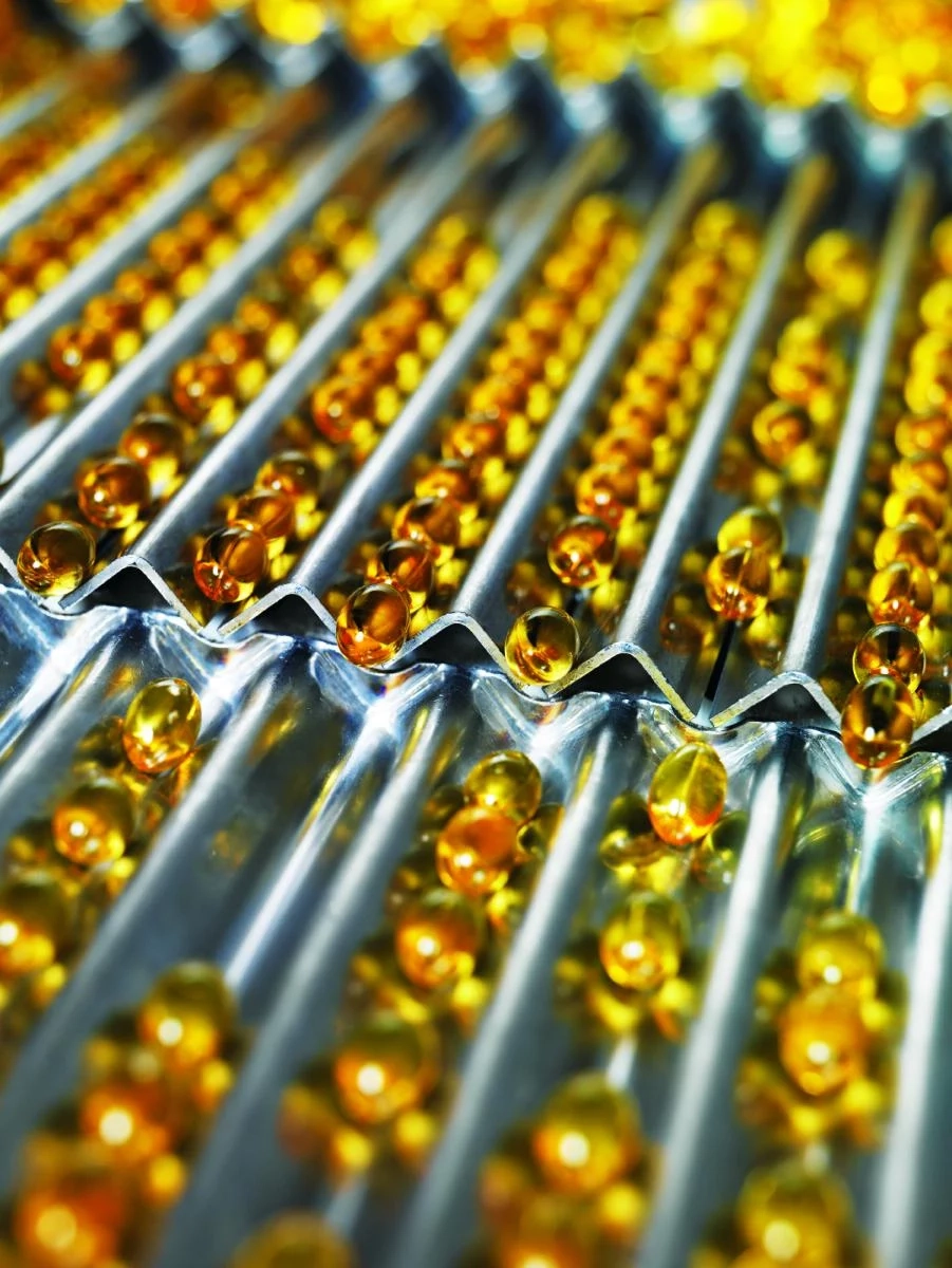 Close-up of golden gel capsules arranged in rows on a metallic sorting tray.