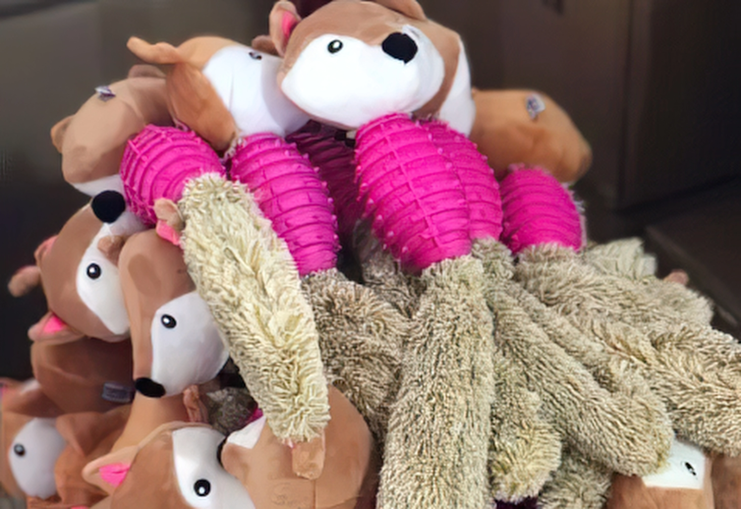 Pile of plush dog toys shaped like foxes with brown heads and bright pink and beige fuzzy bodies.