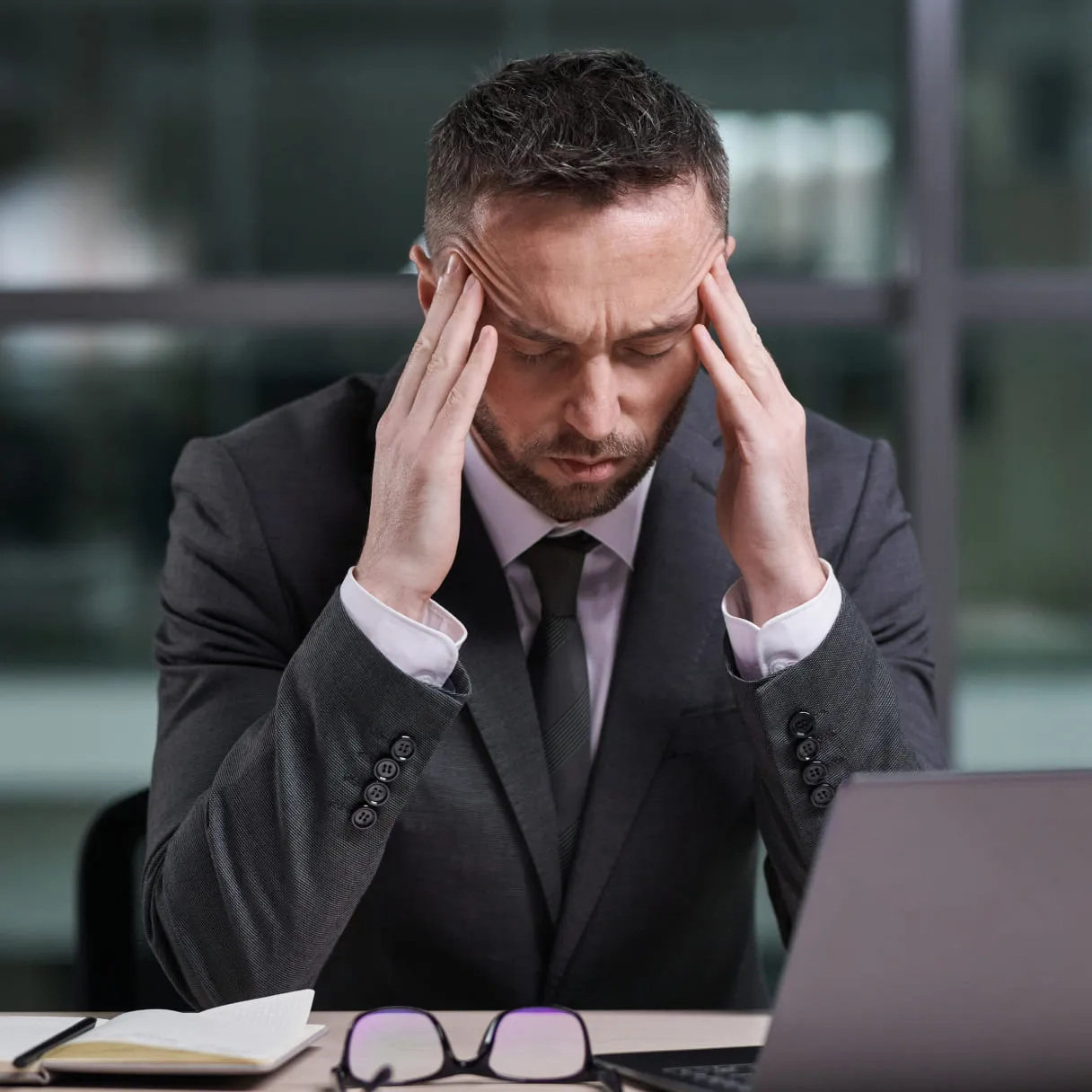 A man sitting at a desk with his hands on his head.
