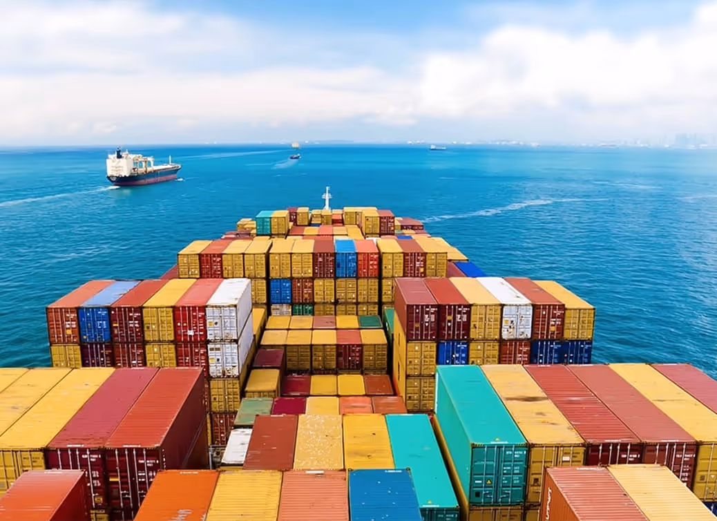 View from a cargo ship deck showing stacked colorful shipping containers with another ship and calm blue sea in the background.