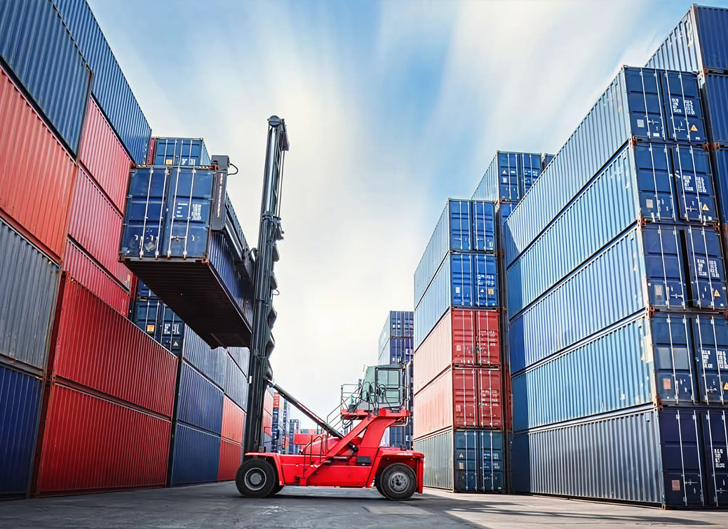 Red forklift lifting a blue shipping container in a busy container yard with stacked red and blue containers.