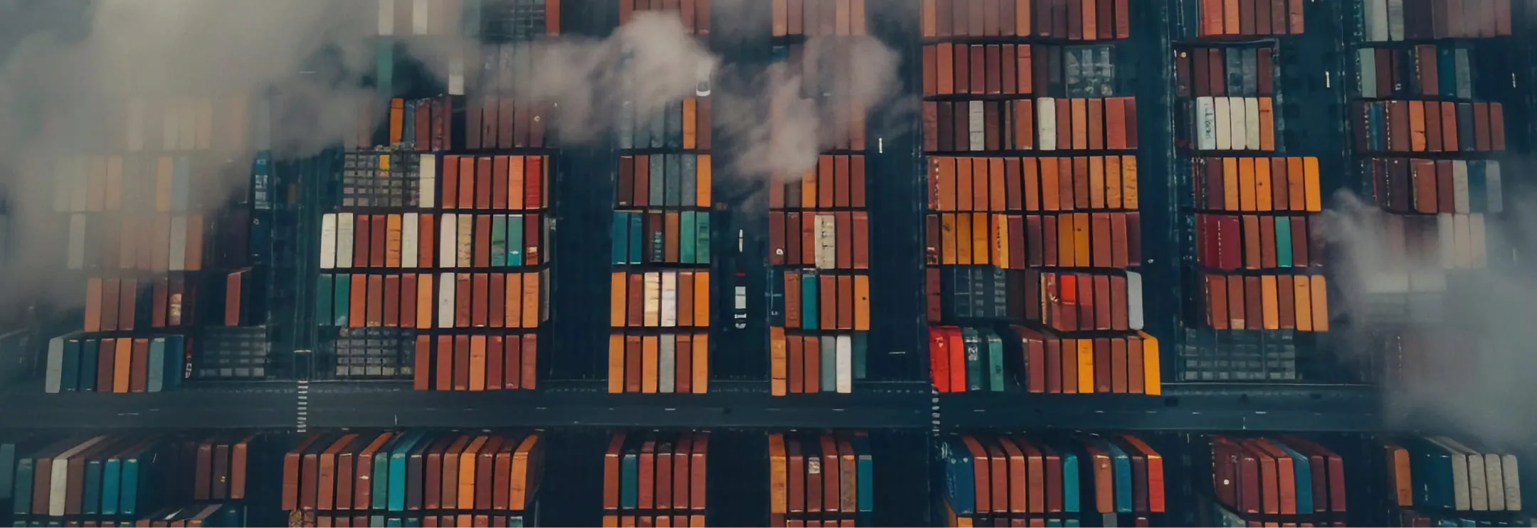 Aerial view of stacked colorful shipping containers at a port with some fog or smoke above.