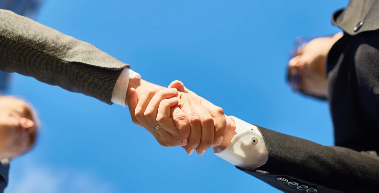 Two business people shaking hands outdoors against a clear blue sky.