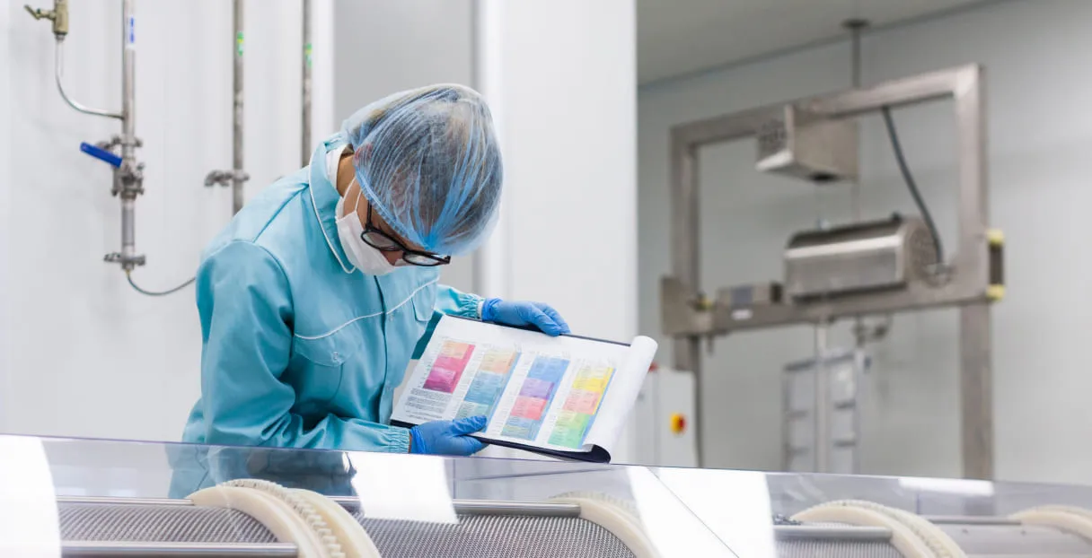 Laboratory worker in protective gear reviewing a color-coded data chart in a clean, industrial setting.
