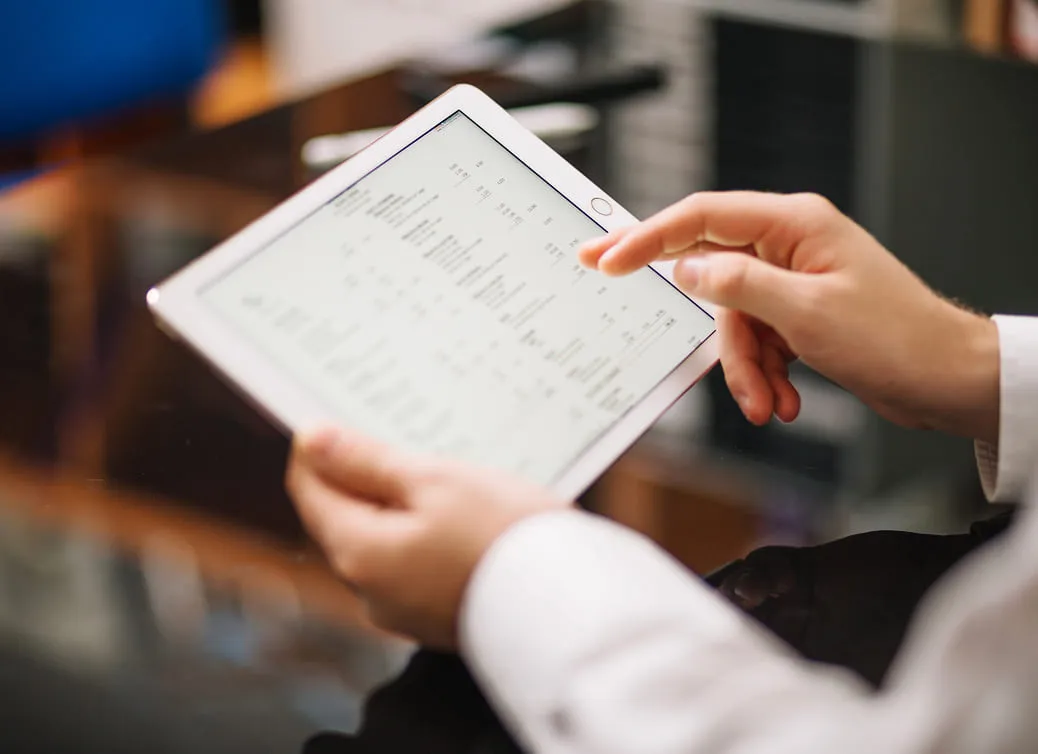 Person holding and interacting with a white tablet displaying a screen of data or chart.