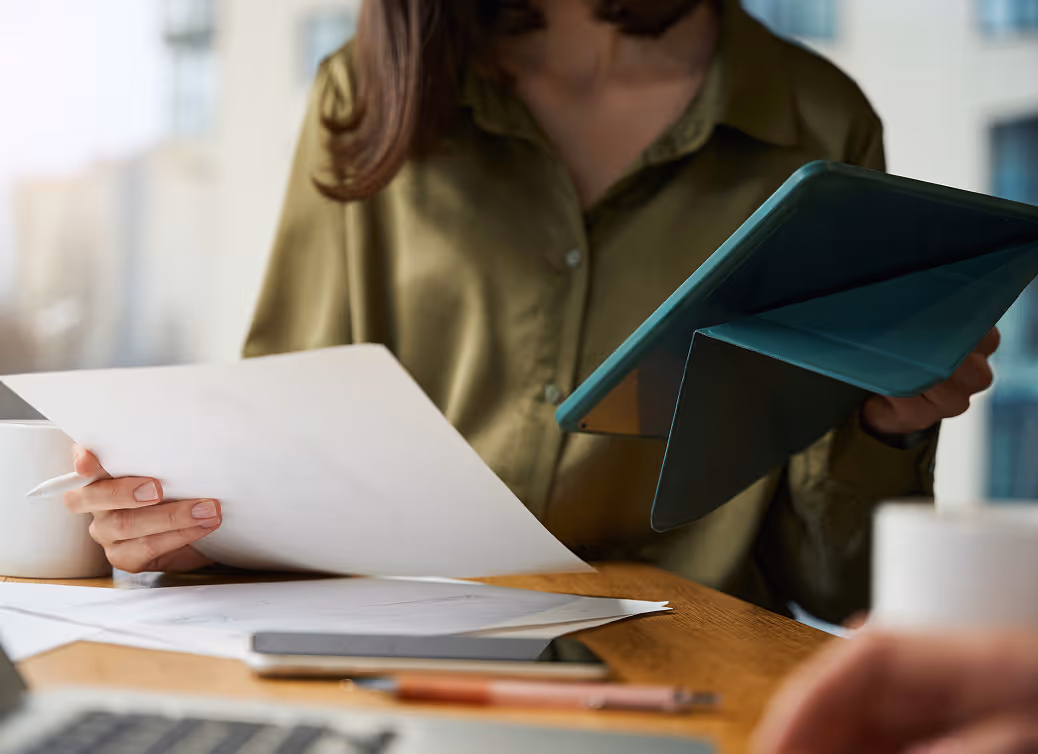 Person in green shirt reviewing documents with a tablet in hand at a wooden table.