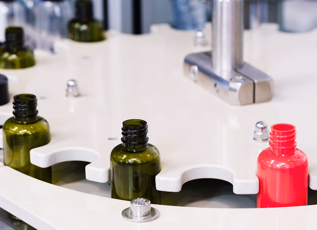 Close-up of green and red glass bottles on a white circular assembly line in a manufacturing facility.