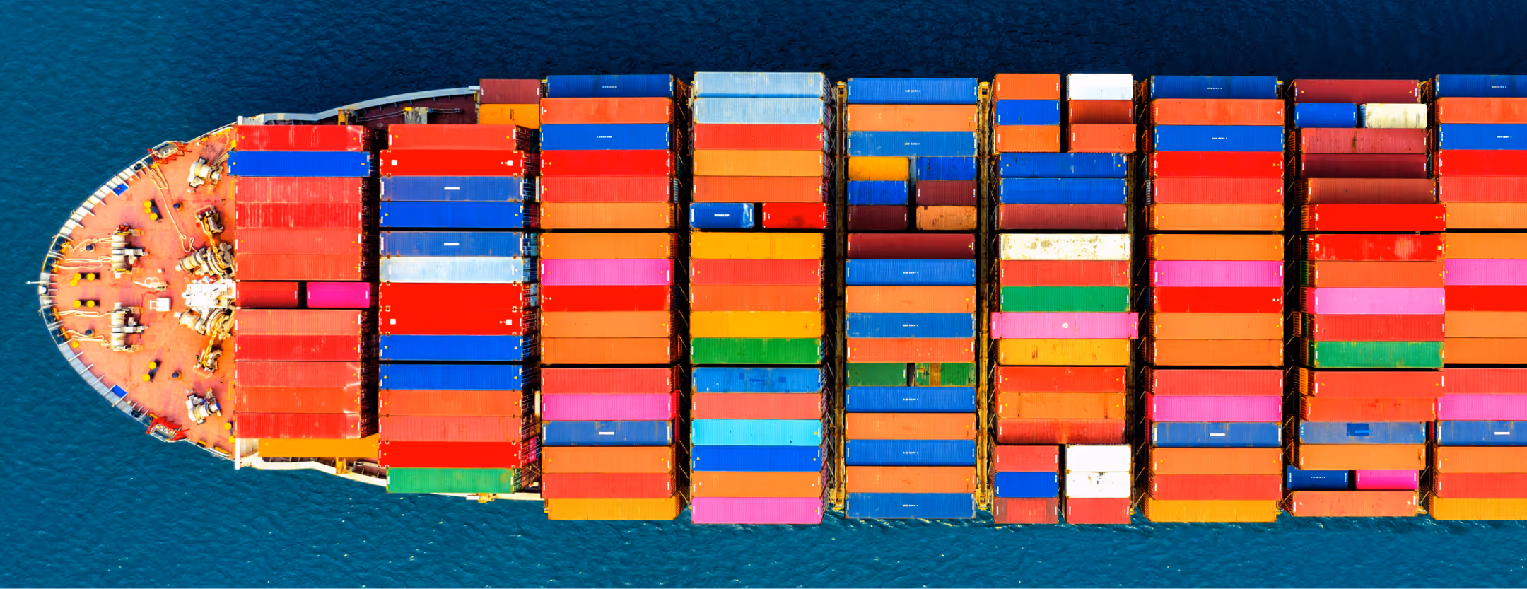Aerial top-down view of a cargo ship loaded with multi-colored shipping containers on blue water.