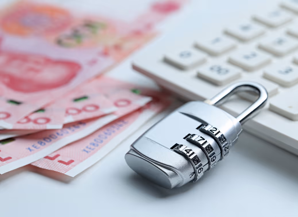 Silver combination lock placed on a white surface next to a keyboard and several pink currency notes.