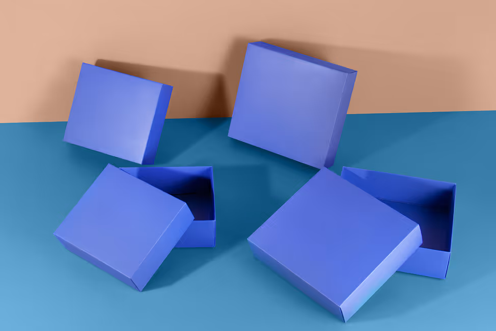 Two blue square gift boxes with lids, one pair smaller and one pair larger, arranged open on a blue surface against a beige background.