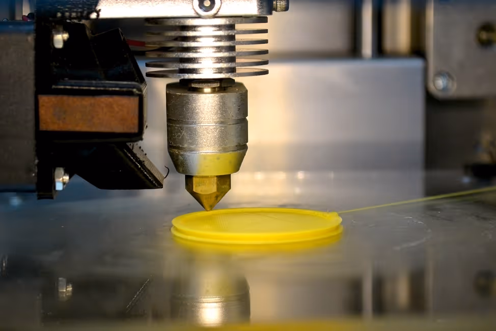 Close-up of a 3D printer nozzle extruding yellow filament to create a circular object.