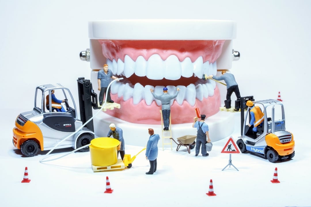 Miniature construction workers and vehicles cleaning and repairing a large model of human teeth and gums.