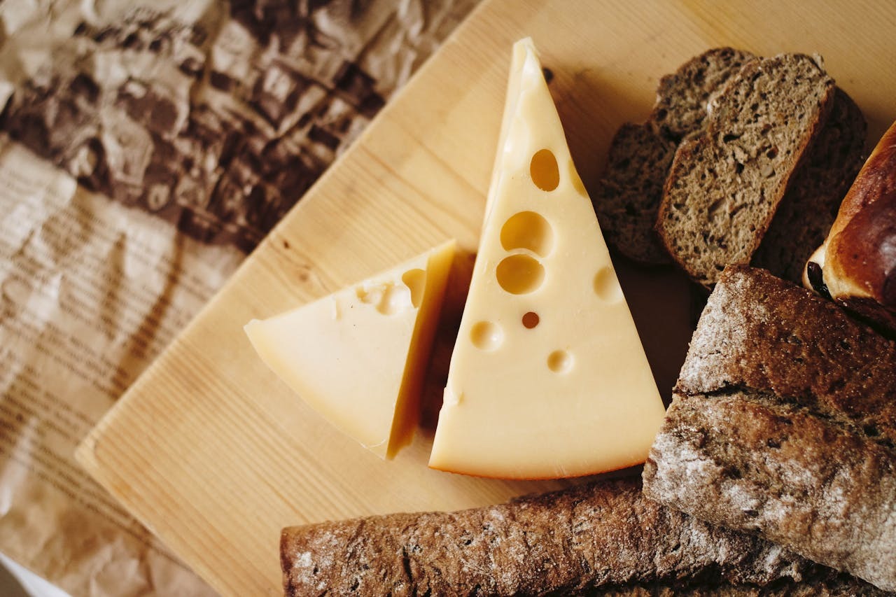 A wooden board with slices of cheese and various types of bread, including dark and light varieties.