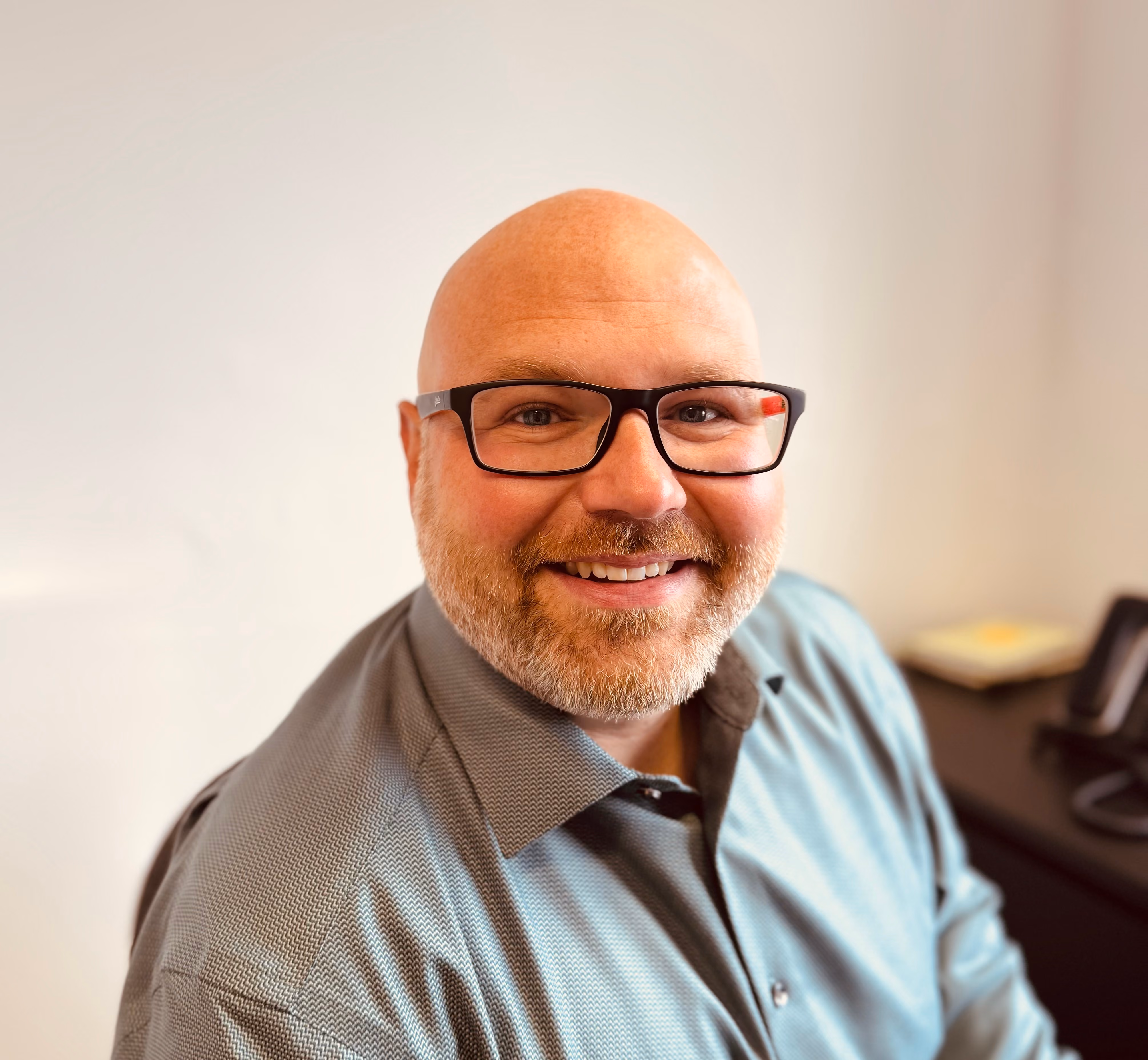 Smiling bald man with red beard wearing glasses and light blue shirt