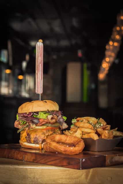 Tall burger with fries and onion rings