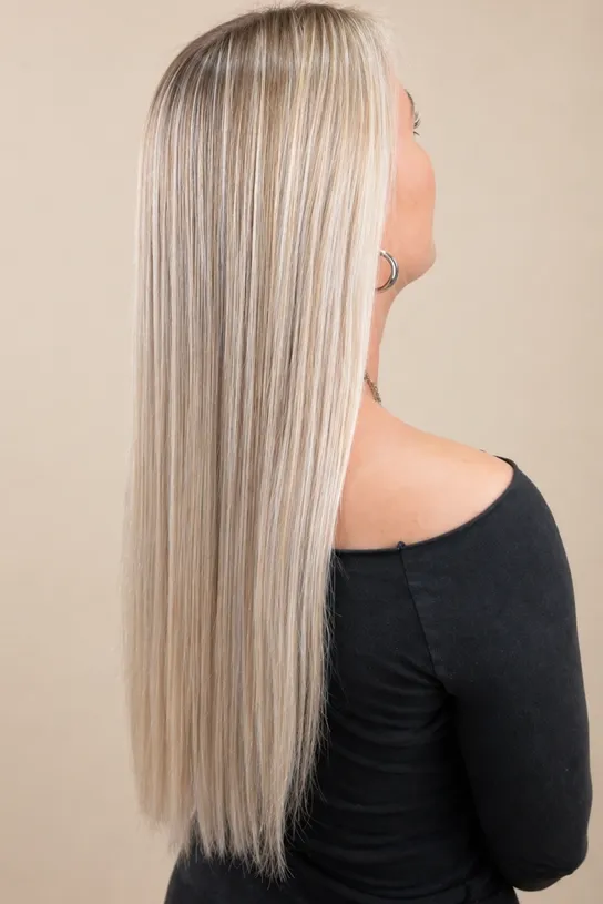 Woman with long, straight blonde hair with highlights against a beige background.