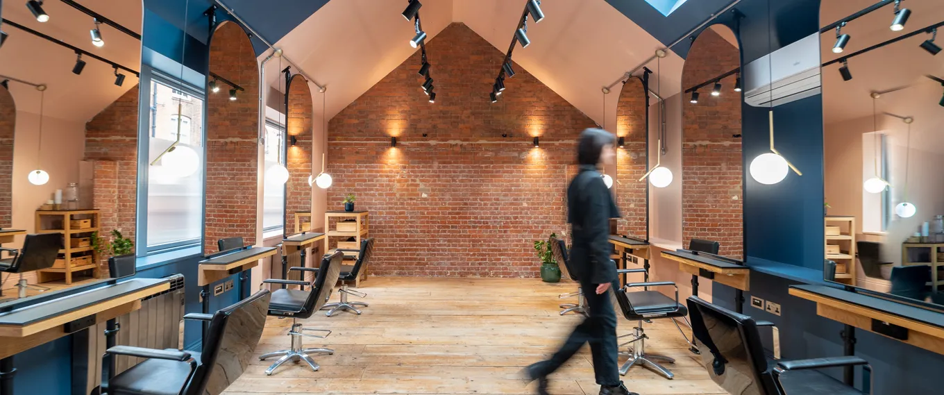 Bond, shoreditch hair salon with brick walls, wooden floors, black styling chairs, large mirrors, and hanging lights.