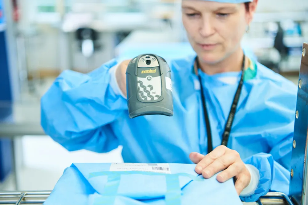 Medicinsk medarbejder i blå kirurgisk kit scanner en emballage med en håndholdt stregkodescanner.